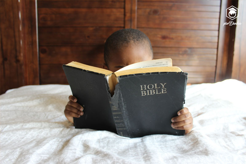 Criança de bruços na cama lendo a bíblia